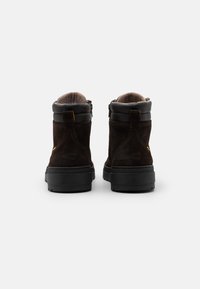 Brown suede ankle boots with black rubber soles, featuring a zip closure and a soft fleece lining. Simple design with minimal accents.