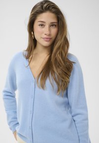 Lichtblauw vest van zacht materiaal, met een V-hals, knoopsluiting en gestikte details aan de linkerkant.