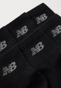 Calcetines negros con textura acanalada, que presentan un logo gris de New Balance en el puño. Diseño simple sin patrones o acentos adicionales.