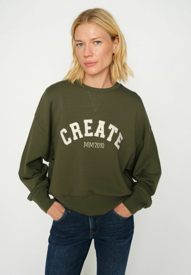 Olivgrön sweatshirt med "CREATE MM2010" tryckt i vitt. Har rund halsringning, neddragna axlar och en avslappnad passform.