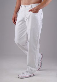 Weiße Denim-Jeans mit lockerer Passform, Five-Pocket-Design und Metallknopfverschluss. Getragen mit weißen Sneakern mit roten Akzenten.