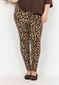 Leggings imprimé léopard dans des teintes beiges et marron, dotés d'un design ajusté et d'une texture lisse, associés à des ballerines en mesh noires.