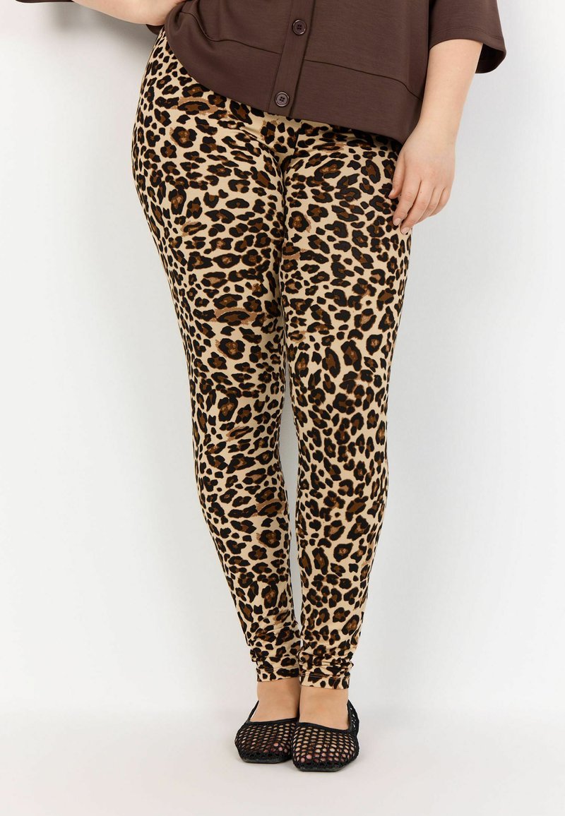 Leggings imprimé léopard dans des teintes beiges et marron, dotés d'un design ajusté et d'une texture lisse, associés à des ballerines en mesh noires.