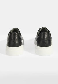 Schwarze Leder-Sneaker mit strukturiertem Finish, ausgestattet mit einer weißen Gummisohle und runder Form. Die Rückansicht zeigt ein Nahtdetail.