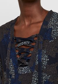 Námořnická modrá blůza s květinovým vzorem a výstřihem do V, která má křížové šněrování a strukturovanou tkaninu.