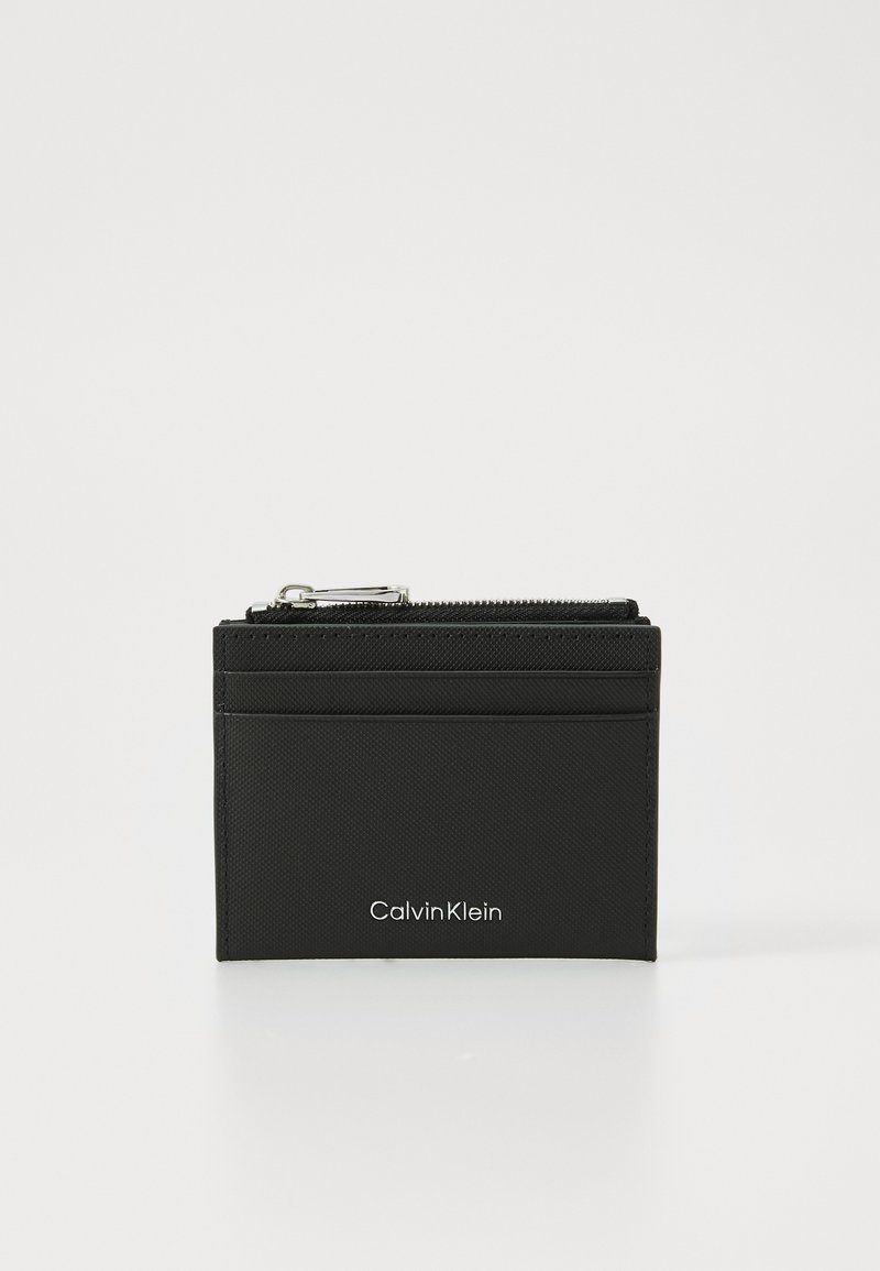 Black zippered wallet made of textured material, featuring a card slot and the Calvin Klein logo in white at the bottom.