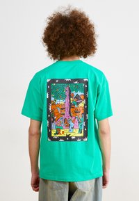 Turquoise cotton t-shirt with a rear graphic featuring vibrant colors and a playful design, framed in black with white accents.