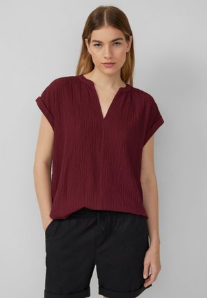 Haut bordeaux à manches courtes avec une surface texturée, décolleté en V et coupe décontractée. Associé à un short noir, avec une taille élastique.
