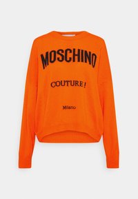 Helle orange Strickjacke mit überschnittenen Schultern, mit schwarzem "MOSCHINO COUTURE!"-Text und gesticktem "Milano"-Detail am Saum.