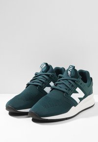 Green mesh sneakers with a white "N" logo, padded collar, and laces. Features a textured upper and a contrasting white outsole.