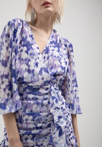 Robe portefeuille florale en violet et blanc, avec des manches bouffantes, des détails en volants et un tissu froncé pour plus de texture.