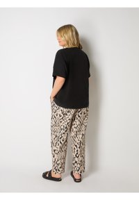 Svart t-shirt med kort ärm i kombination med beiga mönstrade vida byxor med svarta abstrakta mönster, har sidofickor och platta sandaler.