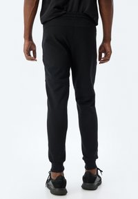 Sorte sweatpants med tekstureret stof, tætsiddende manchetter og elastisk talje, parret med sorte sportssko.