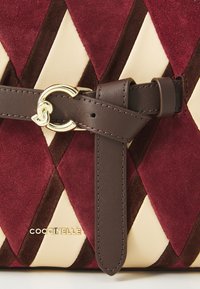 Maroon and beige suede handbag with diamond pattern, featuring a brown leather strap and gold hardware. Logo engraved on the front.
