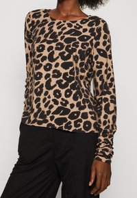 Haut à manches longues en imprimé léopard beige et noir, avec un col rond et des manches ajustées, fabriqué en matériau textile doux.