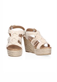 Sandalias cuña en blanco roto con tiras de tela trenzadas y plataforma de cuerda texturizada. Diseño de punta abierta con correa en el tobillo ajustable.