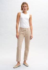 Top in cotone crema, pantaloni beige con coulisse e scarpe basse beige chiaro, esposti su uno sfondo neutro.