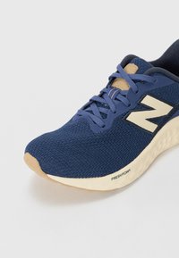 Navy mesh running shoe with beige accents, featuring a structured design, laces, and a rubber sole labeled "FRESH FOAM."