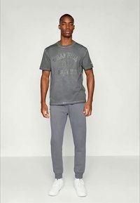 Pilkas medvilnės marškinėlis su išblukusia spauda ir apvaliu iškirpimu, derinamas su pilkais sportiniais džinsais ir baltais sportbačiais. Paprastas dizainas, laisvas kirpimas.