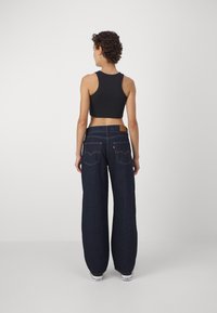 Tamsiai mėlyni, plačių kojų džinsai su aukštu liemeniu, turintys užpakalines kišenes, odinę etikėtę ant liemens, bei siuvimo detales. Sukomplektuoti su juodu trumpu viršumi.