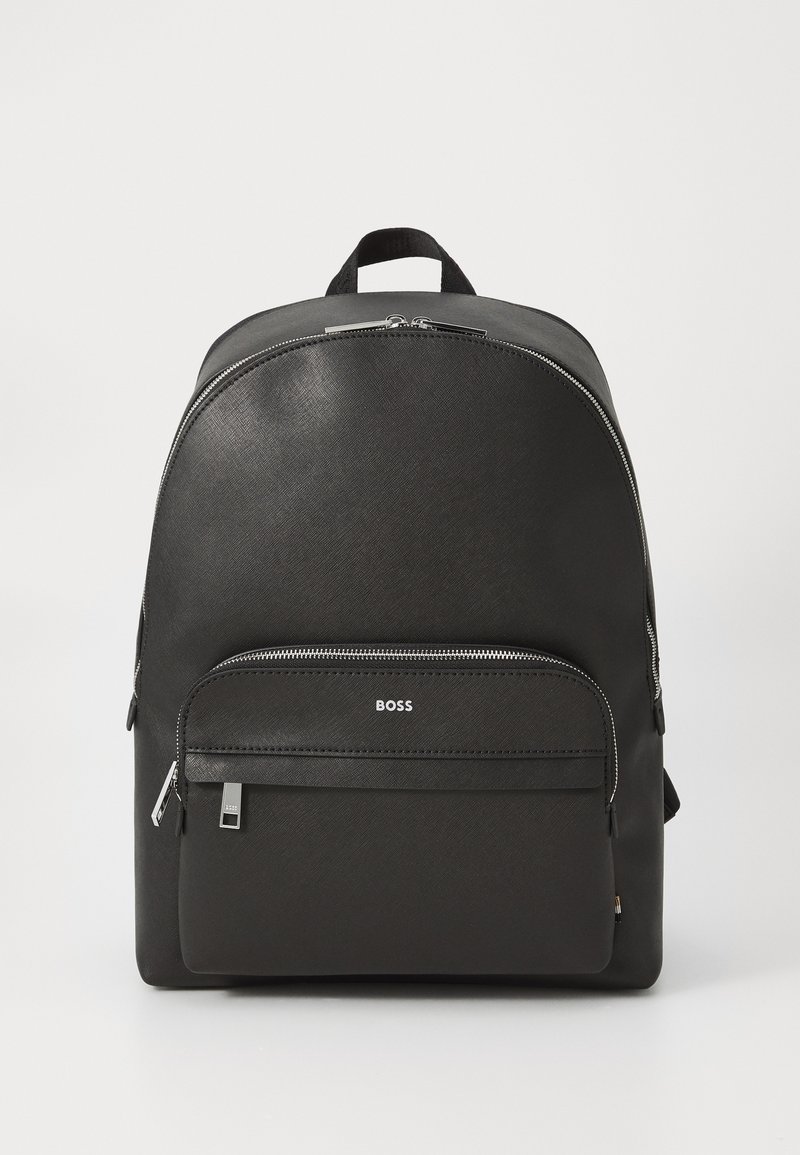 Sac à dos noir avec une surface lisse et texturée, doté d'une poche zippée à l'avant et du nom de la marque "BOSS" en relief sur la poche inférieure.