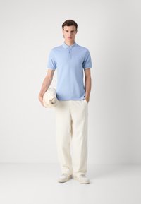 Polo shirt azzurro chiaro con accenti bianchi, maniche corte e un piccolo logo sul petto. Abbinato a pantaloni larghi di colore crema e sneakers bianche.