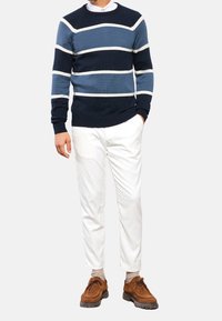 Marinblå och ljusblå randig stickad tröja med rund hals, kombinerad med vita byxor och bruna mockaskor. Texturerad, avslappnad stil.