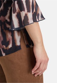 Haut fluide et à motifs avec des tons bleu marine, marron et crème. Présente des manches volantées et un tissu texturé et léger.