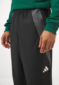 Pantalones deportivos negros con un panel de acento gris, cinturilla elástica y logo blanco. Tejido suave con un diseño ajustado.