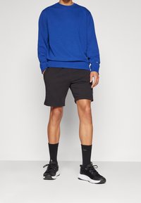 Blå sweatshirt med rund hals och svarta träningsshorts. Svarta strumpor och sneakers kompletterar outfiten. Avslappnad sportig stil.