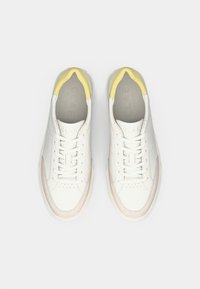 Sneakers bianchi in pelle con un accento giallo sul tallone, caratterizzati da una finitura liscia, punta perforata e cuciture tonali, design con lacci.