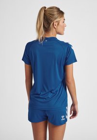 Blå atletisk t-shirt og shorts lavet af glat, åndbart stof. T-shirten har korte ærmer, og shortsene har et logo ved kanten.