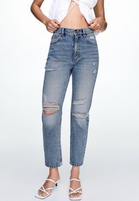 Höga ljusblå denimjeans med slitna hål vid knäna, rak passform och fransade fållar. Avslutad med klassisk femfickdesign.