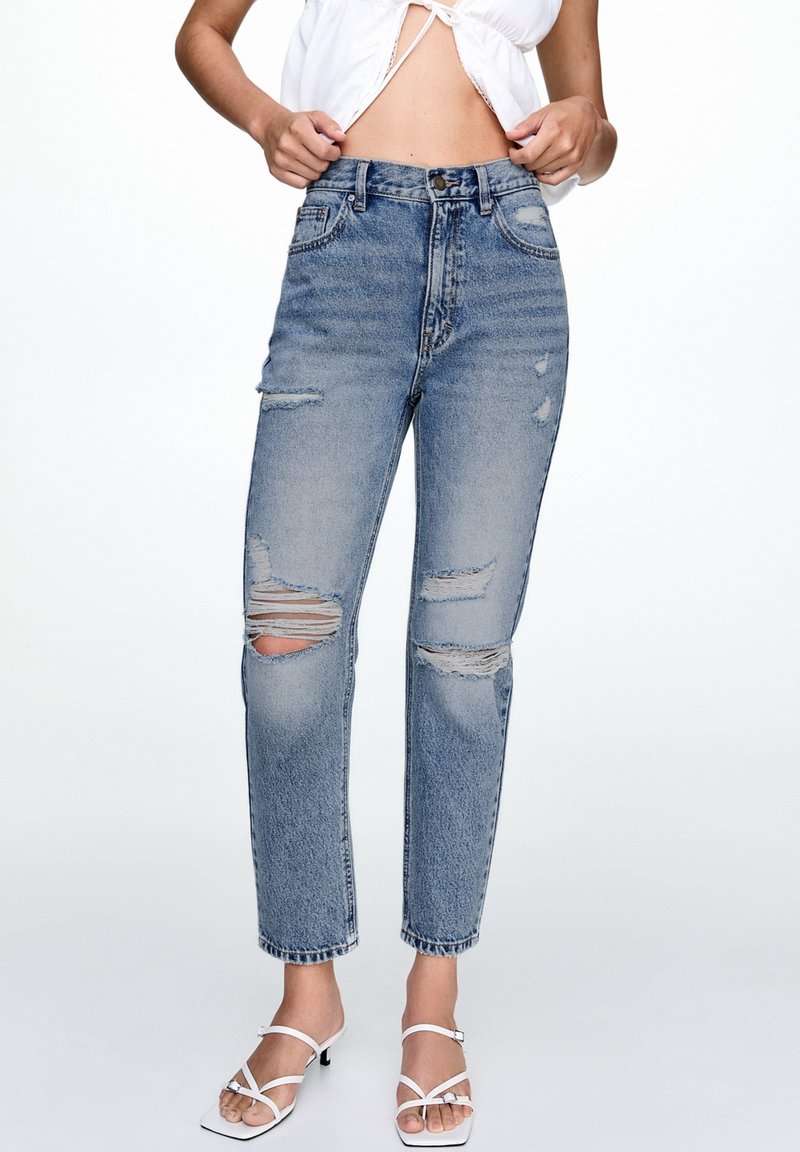 Höga ljusblå denimjeans med slitna hål vid knäna, rak passform och fransade fållar. Avslutad med klassisk femfickdesign.