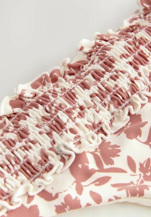 Blomsterprintet stof i creme og støvet rosenfarve med samlede teksturer og bølgede kanter, der fremhæver fine detaljer og blødt materiale.