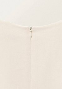 Kermanvärinen kangas, jossa on sileä rakenne, piilonvetoketju takana ja pystysuora sauma keskilinjassa.