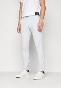 Világosszürke, slim fit pamut nadrág, gombos zárással és finom varrási részletekkel, fehér sportcipővel párosítva.