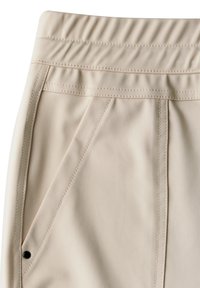 Beige Hose mit elastischem Bund, schräger Seitentasche, sichtbaren Nähten und kleinem schwarzen Nieten an der Ecke der Tasche.