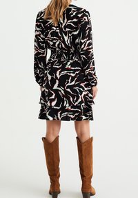 Black dress with abstract white, green, and orange patterns; long sleeves, smocked waist, ruffled hem, paired with brown suede knee-high boots.