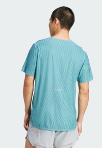 Camiseta deportiva azul verdoso de manga corta, con un patrón de rayas texturizado y detalles reflectantes. Corte holgado con un diseño liso en la parte trasera.