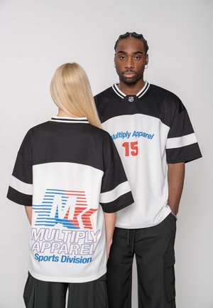 Man and woman wearing black and white sports jerseys with "Multiply Apparel" branding; man faces forward, woman shows back of jersey.
