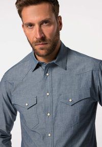 Modrá džínová košile s špičatým límcem, dvěma náprsními kapsami, bílými patentkami a texturovaným materiálem. Obsahuje design yoky ve westernovém stylu.