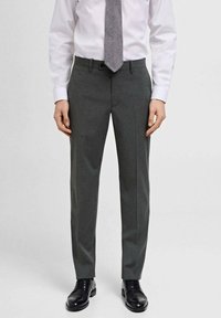 Pantaloni gri din material texturat, cu o croială ajustată și pliuri călcate. Purtați cu o cămașă albă și o cravată cu model. Pantofi negri din piele.