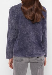 Lila, langärmliges Oberteil mit einer weichen, strukturierten Oberfläche. Lässiger Schnitt mit einem runden Ausschnitt. Graue Denim-Hosen mit Details an der Gesäßtasche.