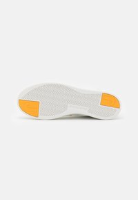 Weiße Sneaker-Sohle mit Fischgrätenstruktur und gelbem Akzent. Gummimaterial, flache Form und verstärktes Fersenbereich.