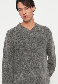 Grå, v-hals genser laget av mykt strikkemateriale med teksturert overflate. Avslappet passform, lange ermer og minimalistisk design.