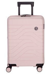 Valigia rigida rosa con un design testurizzato ondulato, manico retrattile nero e quattro ruote multidirezionali per una facile mobilità.