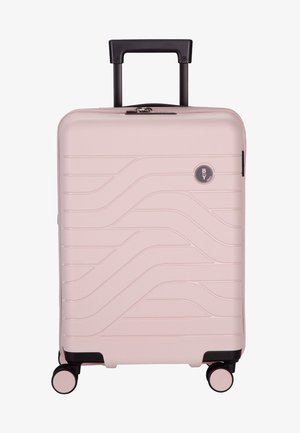 Valigia rigida rosa con un design testurizzato ondulato, manico retrattile nero e quattro ruote multidirezionali per una facile mobilità.