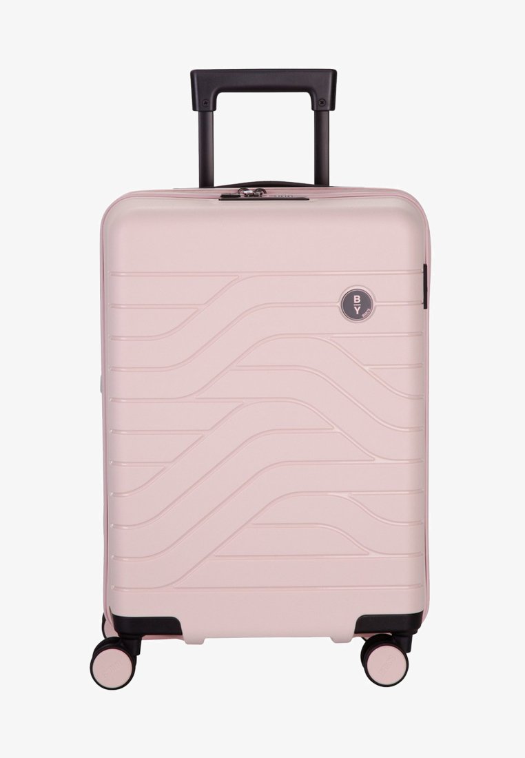 Valigia rigida rosa con un design testurizzato ondulato, manico retrattile nero e quattro ruote multidirezionali per una facile mobilità.