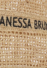 Geweven straw tas in beige met een open structuur. Bevat zwart geborduurde tekst met "VANESSA BRUNO," wat contrast toevoegt aan het ontwerp.